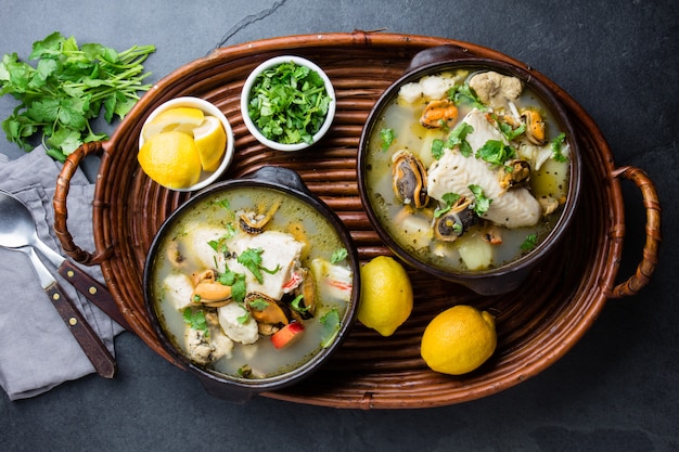Sopa de pescado y marisco en cuencos de barro servido con limón y cilantro.