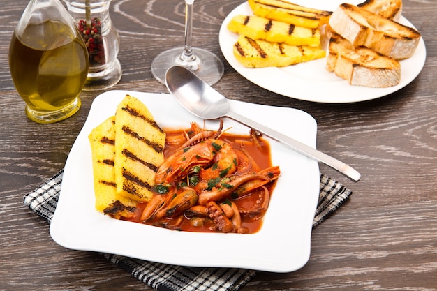 Sopa de pescado con polenta a la parrilla en un plato blanco.