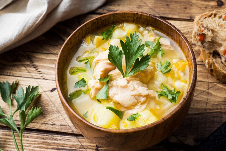 Sopa de pescado en un recipiente de madera con hierbas frescas.