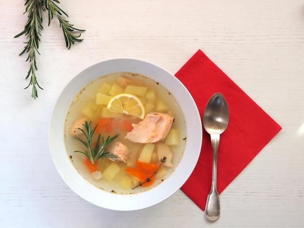 Sopa de pescado con romero y servilleta roja servida en mesa blanca Lay Flat