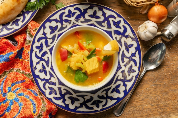 Sopa de pescado de salmón, cebollas, tomates, ajo, zanahorias, patatas, eneldo, especias y limón en un plato con adornos tradicionales de Uzbekistán