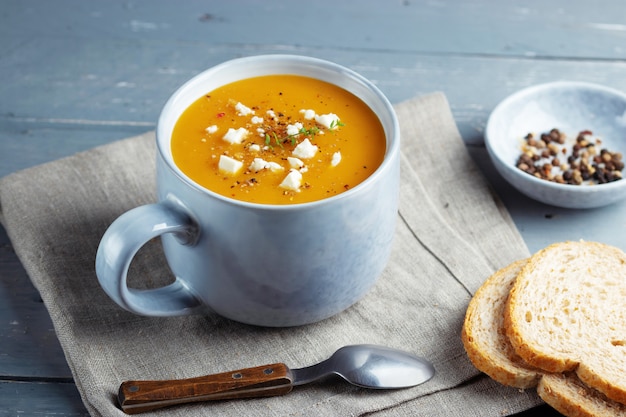 Sopa picante de calabaza y camote en una gran taza de cerámica adornada con queso feta.