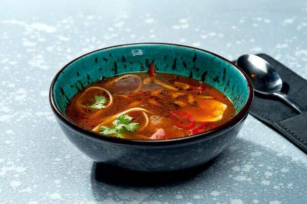 Sopa picante de ramen pan-asiática com macarrão, carne, pimenta e coentro em uma tigela azul sobre uma superfície cinza