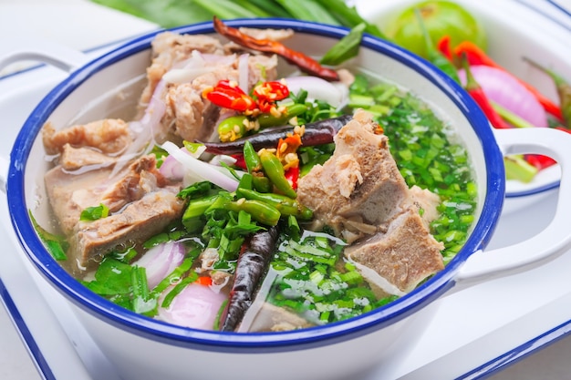 Sopa picante de hueso de cerdo al estilo tailandés Es una sopa clara de hueso de cerdo con grandes huesos de cerdo, decorada con chile y hierbas tailandesas.