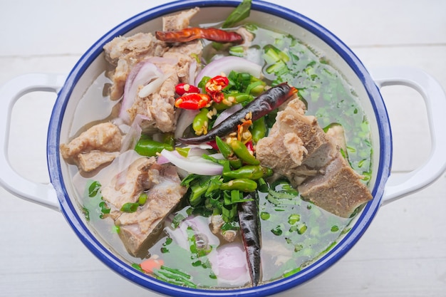 Sopa picante de hueso de cerdo al estilo tailandés Es una sopa clara de hueso de cerdo con grandes huesos de cerdo, decorada con chile y hierbas tailandesas.