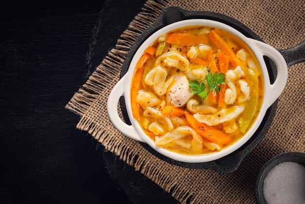 Sopa de pollo casera rusa con fideos y verduras en un plato blanco sobre un fondo negro