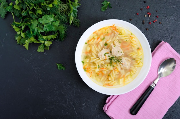 Sopa de pollo dietético con fusilli en un recipiente blanco sobre un fondo negro. La vista superior