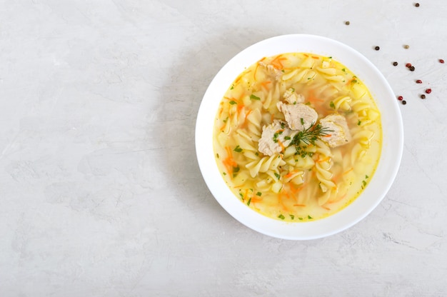 Sopa de pollo dietético con fusilli en un tazón blanco sobre un fondo claro. La vista superior Copia espacio