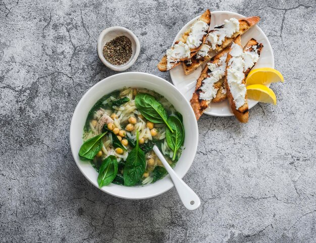 Sopa de pollo con espinacas orzo al estilo griego sobre fondo gris vista superior Deliciosa comida reconfortante