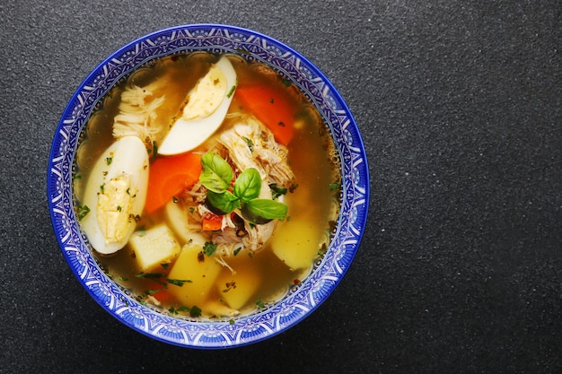 Sopa de pollo con fideos con huevo, verduras y carne de pollo en la vista superior de la mesa oscura