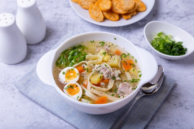 Sopa de pollo, fideos, patatas, huevos de codorniz y zanahorias. Condimentado con cebolla y perejil. De cerca.