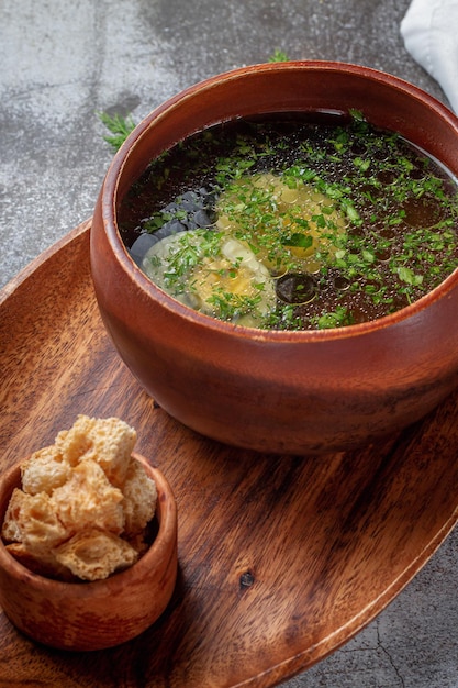 Sopa de pollo con huevo cocido espolvoreado con eneldo y hojas de perejil en un cuenco de madera con pan rallado se encuentra aislado en una mesa de piedra, Flatlay