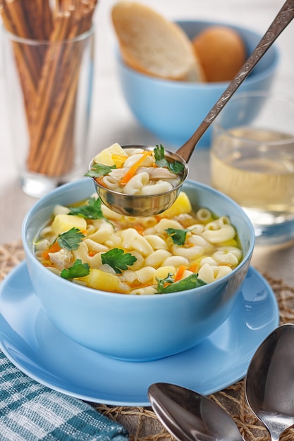 Sopa de pollo con pasta y una rodaja de limón.