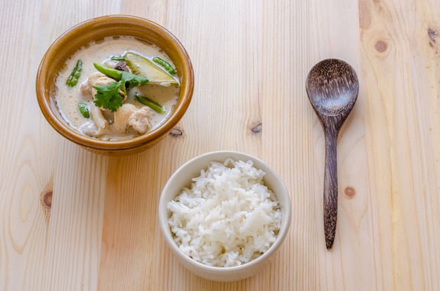 Sopa de pollo tailandesa en la leche de coco (tom kha gai) con arroz en el fondo de madera, comida tailandesa.