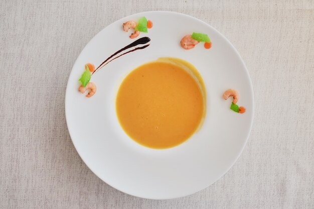 Sopa poner crema vegetal con la zanahoria en el cuenco blanco. Vista superior sobre un paño blanco áspero.
