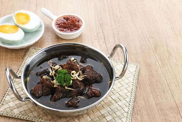 Sopa preta de carne tradicional da Indonésia de Rawon servida em uma tigela com pasta de pimenta de brotos de feijão mungo
