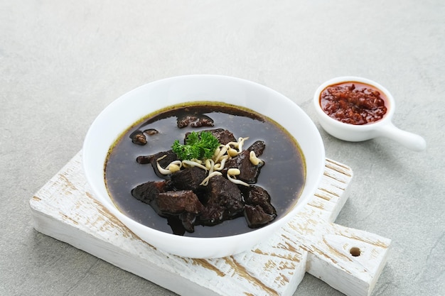 Sopa preta de carne tradicional indonésia de Rawon servida em uma tigela com pasta de pimenta de brotos de feijão mungo