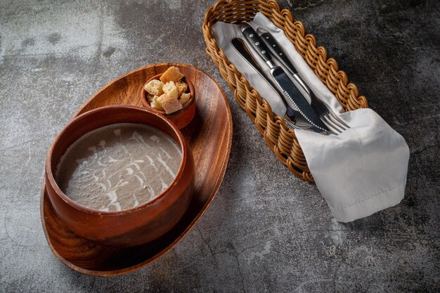 Sopa purê de cogumelos em uma tigela de madeira em uma bandeja com migalhas de pão sobre uma mesa de pedra cinza
