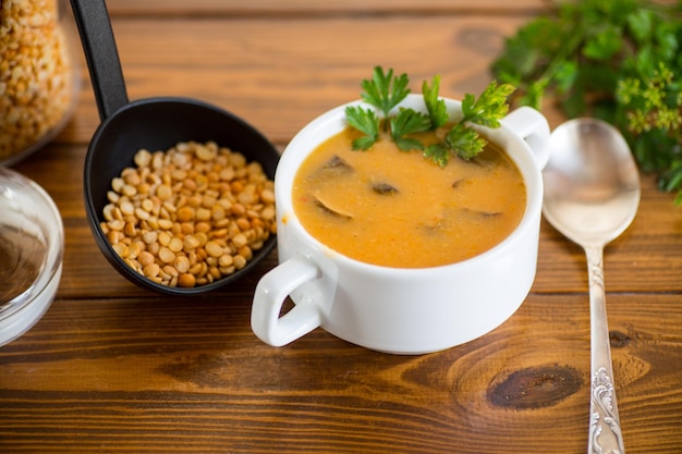Sopa de puré de guisantes secos cocidos con champiñones en un recipiente sobre una mesa de madera oscura
