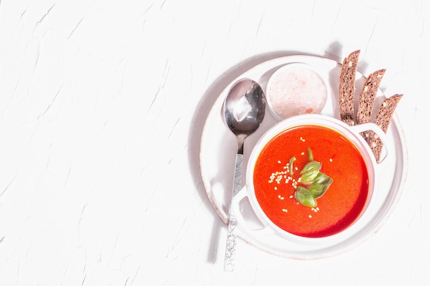 Sopa de puré rojo con tomate, verduras y pan. Luz dura de moda, sombra oscura. Fondo de masilla blanca, vista superior