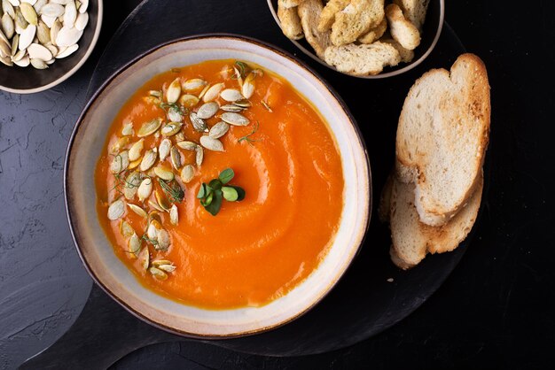 Sopa de puré de verduras de acción de gracias, sopa de crema de calabaza vegetariana en un recipiente sobre un fondo negro, primer plano.