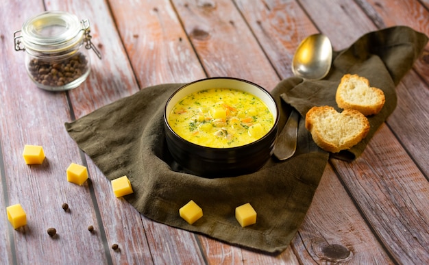 Sopa de queso amarillo en un plato oscuro. Trozos de queso y pan alrededor del plato.