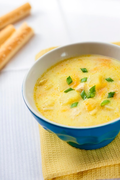 Sopa de queso con pollo, patatas y cúrcuma con grissini sobre un fondo