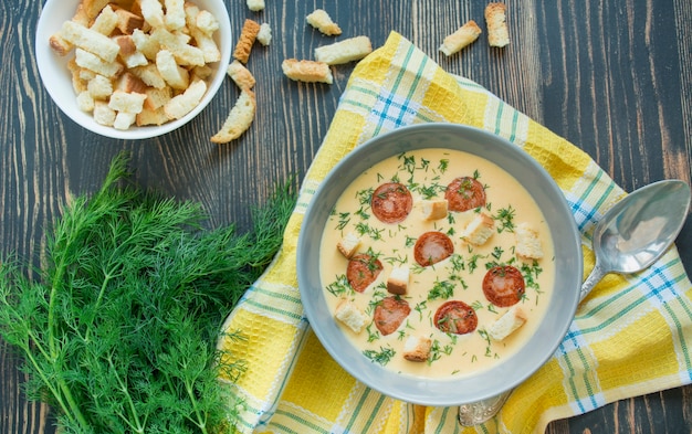 Sopa de queso con salchichas fritas y hierbas. Sabrosa sopa de queso crema en un plato blanco. Mesa del comedor. El equilibrio de una alimentación saludable. Copia espacio Fondo de madera