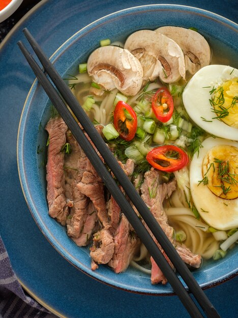 Sopa de ramen asiático con carne de res, huevo, cebollino y champiñones en un tazón.