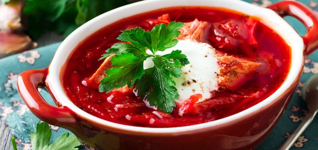 Sopa de remolacha con carne, crema agria y perejil en un cuenco de cerámica marrón sobre el fondo de madera vieja. Borsch- plato tradicional de la cocina ucraniana. Enfoque selectivo.