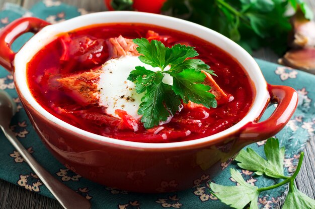 Sopa de remolacha con carne, crema agria y perejil en cuenco de cerámica marrón