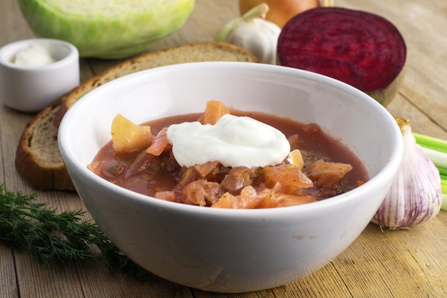 Sopa roja de remolacha rusa en un tazón blanco sobre la mesa de madera de cerca