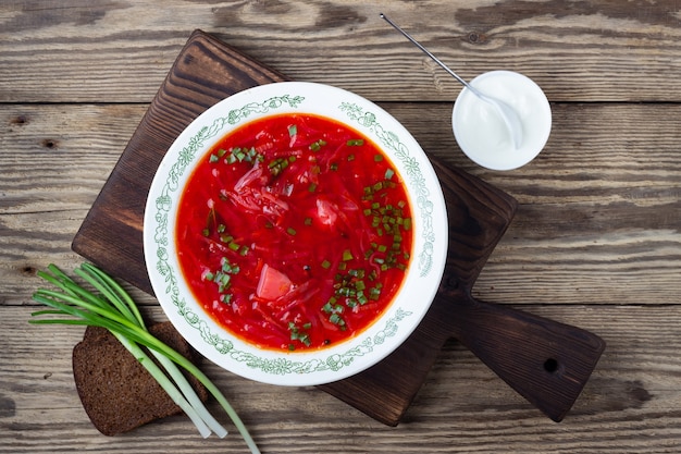 Sopa roja de remolacha vegetariana ucraniana tradicional - borscht con crema agria sobre fondo de madera.