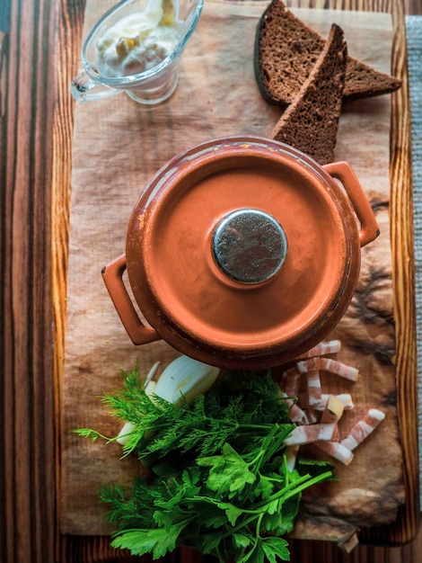 Sopa russa em uma panela de barro ao lado de pão creme de leite verde banha na mesa de madeira