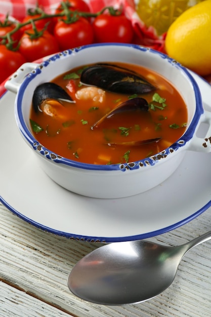 Foto sopa sabrosa con camarones mejillones tomates y aceitunas negras en un cuenco sobre fondo de madera