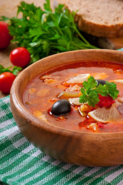 Sopa solyanka russo com carne, azeitonas e pepinos em uma tigela de madeira