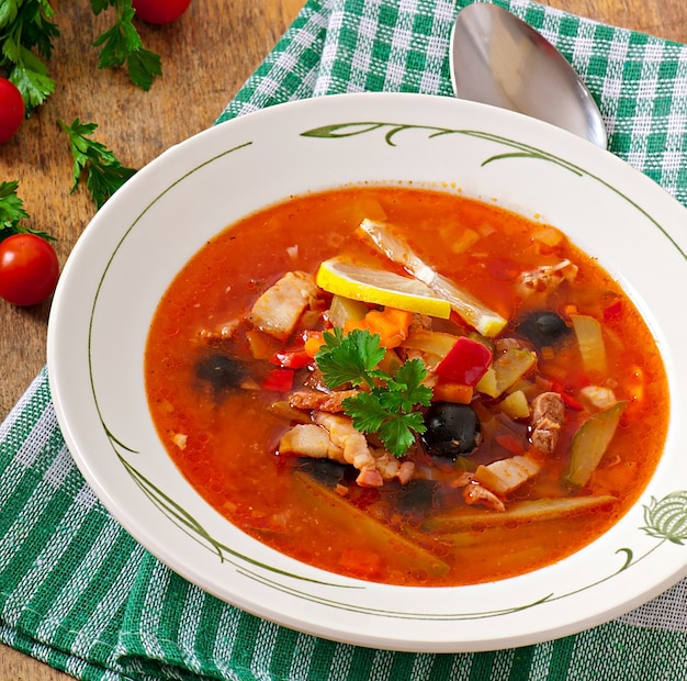 Sopa solyanka russo com carne, azeitonas e pepinos em uma tigela de madeira