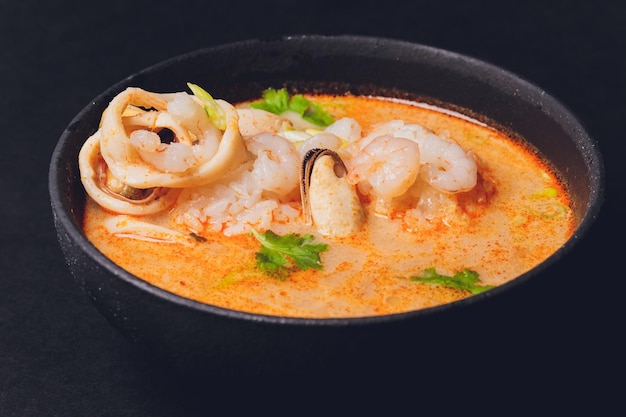 Sopa tailandesa picante Tom Yam con leche de coco Pimienta picante y camarones de marisco y salmón en un plato sobre un menú de restaurante de cocina asiática de fondo negro