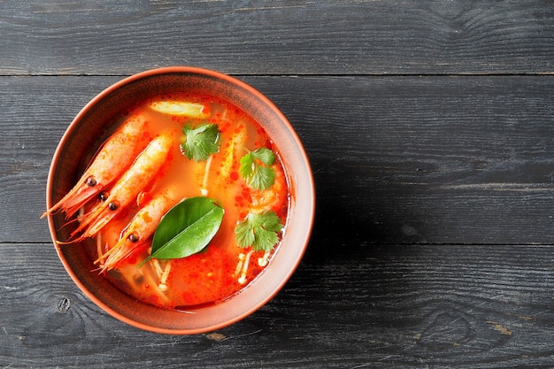 Sopa tailandesa tom yam con camarones, limoncillo y lima en una vista superior de la mesa de madera.