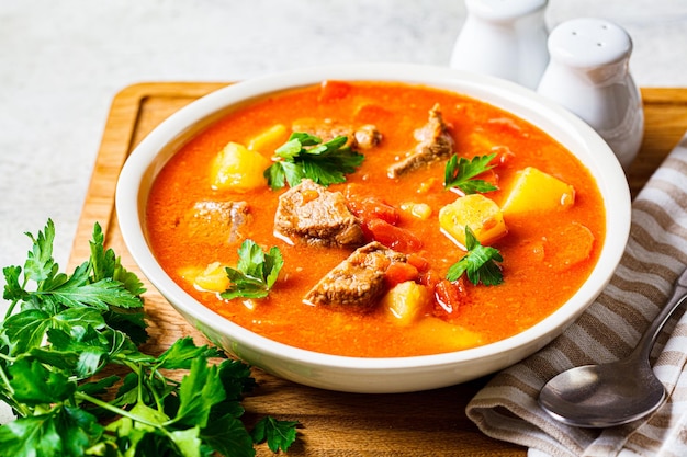 Sopa con ternera y verduras en un plato blanco sobre una tabla de madera Sopa tradicional de shurpa de carne con verduras y hierbas