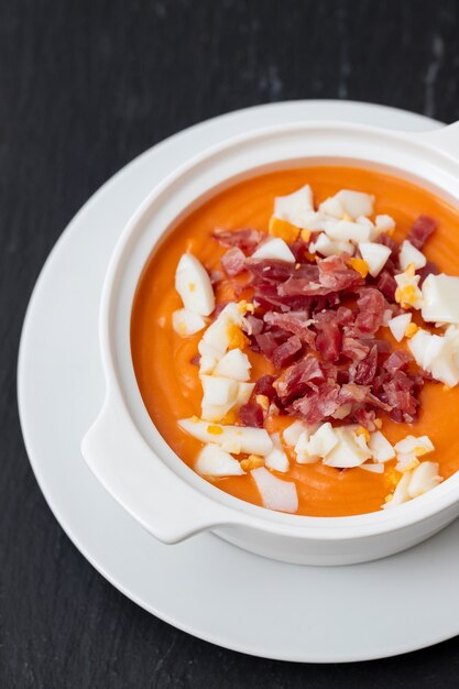 Sopa típica espanhola de creme de salmorejo com presunto e ovo em uma tigela branca sobre fundo de cerâmica