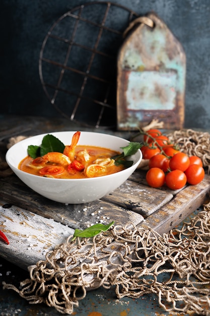 Sopa de Tom Yam con camarones, calamares y pimientos picantes en una tabla de madera con textura.