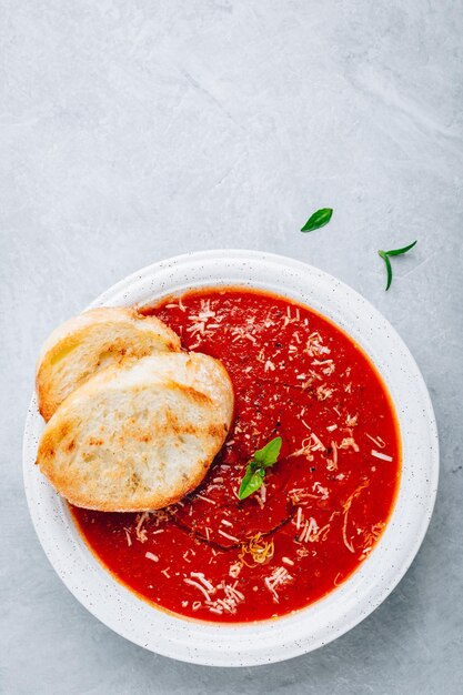 Sopa de tomate y albahaca con queso parmesano y tostadas de pan en la vista superior de fondo de piedra gris