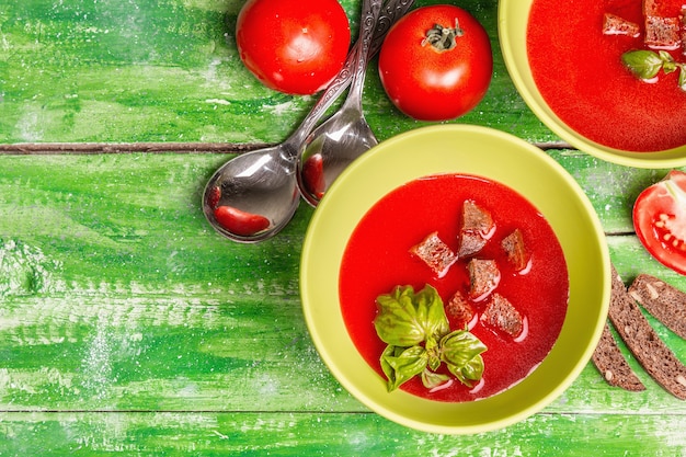 Sopa de tomate con albahaca en tazones. Verduras maduras, verduras frescas, especias aromáticas. Mesa de madera