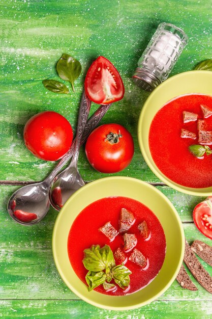 Sopa de tomate con albahaca en tazones. Verduras maduras, verduras frescas, especias aromáticas. Mesa de madera