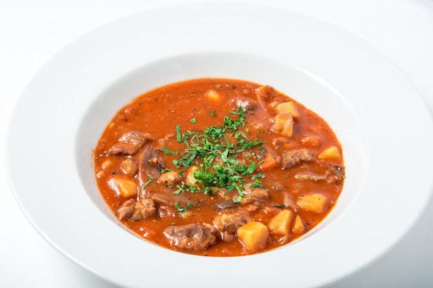 Sopa de tomate con carne, patatas, zanahorias y chirivía en plato blanco