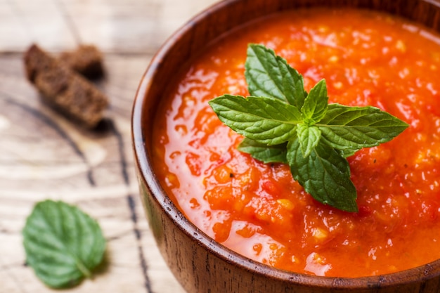 Sopa del tomate en un cuenco de madera con los pedazos de tostada en una tabla rústica.