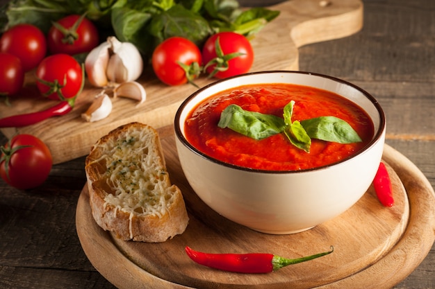 Sopa de tomate fresca y saludable con albahaca, pimiento, ajo, tomate y pan en madera