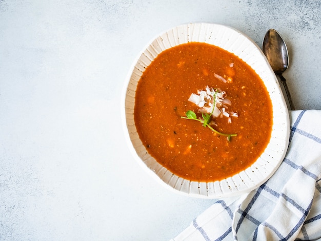 Sopa de tomate fresco con queso y guisantes frescos brotan en un tazón rústico blanco sobre gris