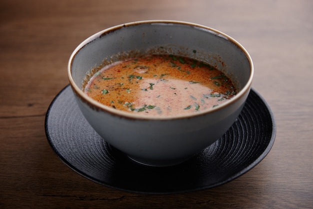 Sopa de tomate con hierbas en un plato de cerámica sobre una mesa de madera oscura.